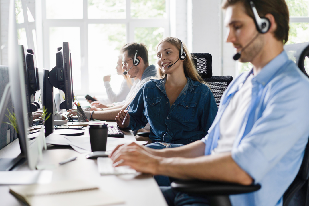 Symbolbild mehrerer Menschen, die Headsets aufhaben und an Computern sitzen